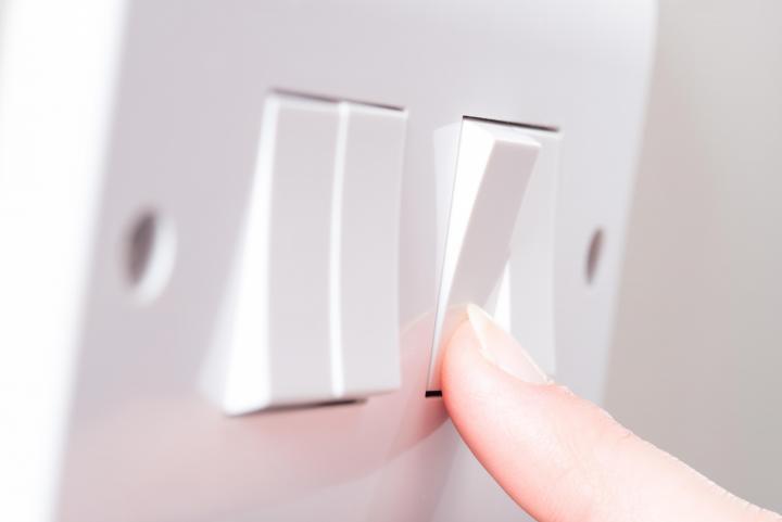Image of a finger pressing a light switch on a wall