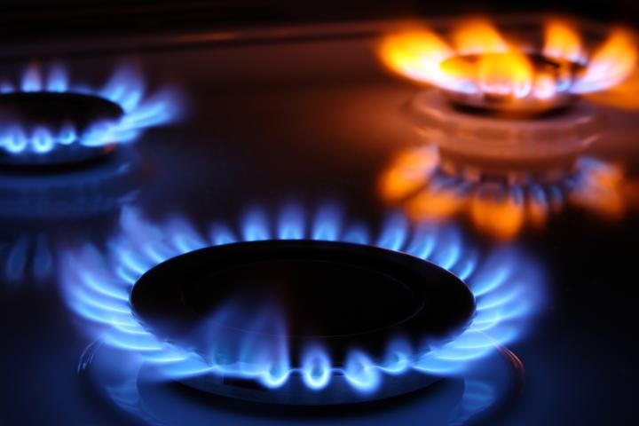 A close-up photo showing three gas burners turned on. Two gas burners are burning blue, while a third is burning orange. 