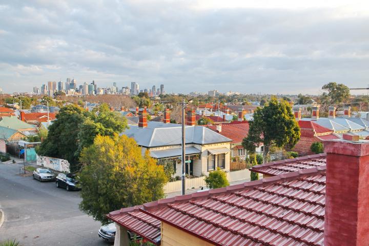 Image showing Melbourne on the horizon, with a suburb sprawling before it. A red roof is in the foreground. 