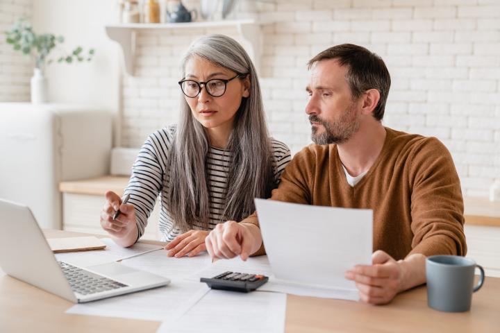 A middle aged couple looking at bills together, at a kitchen table