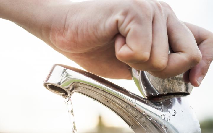 Image of a hand turning off a dripping tap with sunshine in the background