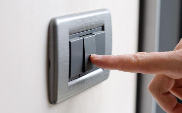 An image showing a hand pressing a grey electric switch on a wall.