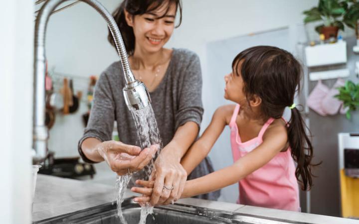 Photo of a mother and daughter at the kitchen sink using tap