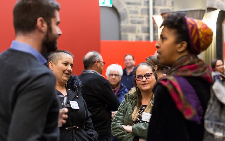 An image of two women (in focus) and a man and woman (foreground, blurred) chatting to each other at the commission's family violence forum on 30 August 2018.